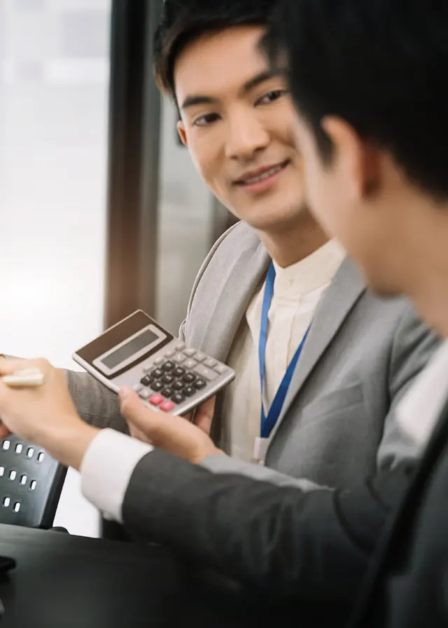Asian men discuss finance in office, using calculator for business teamwork.