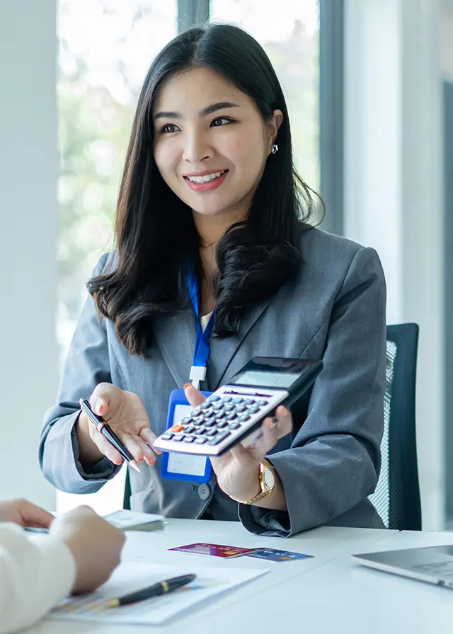 Asian woman provides financial services, holding calculator, in office setting.