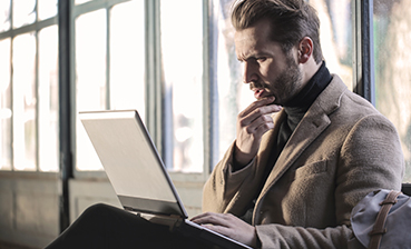 Man contemplating laptop: business professional working, thinking, problem-solving.